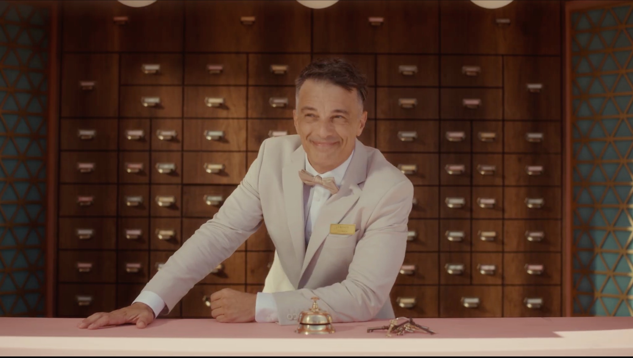 Lorenzo Patane as the Attendant, smiling behind the Lost and Found counter